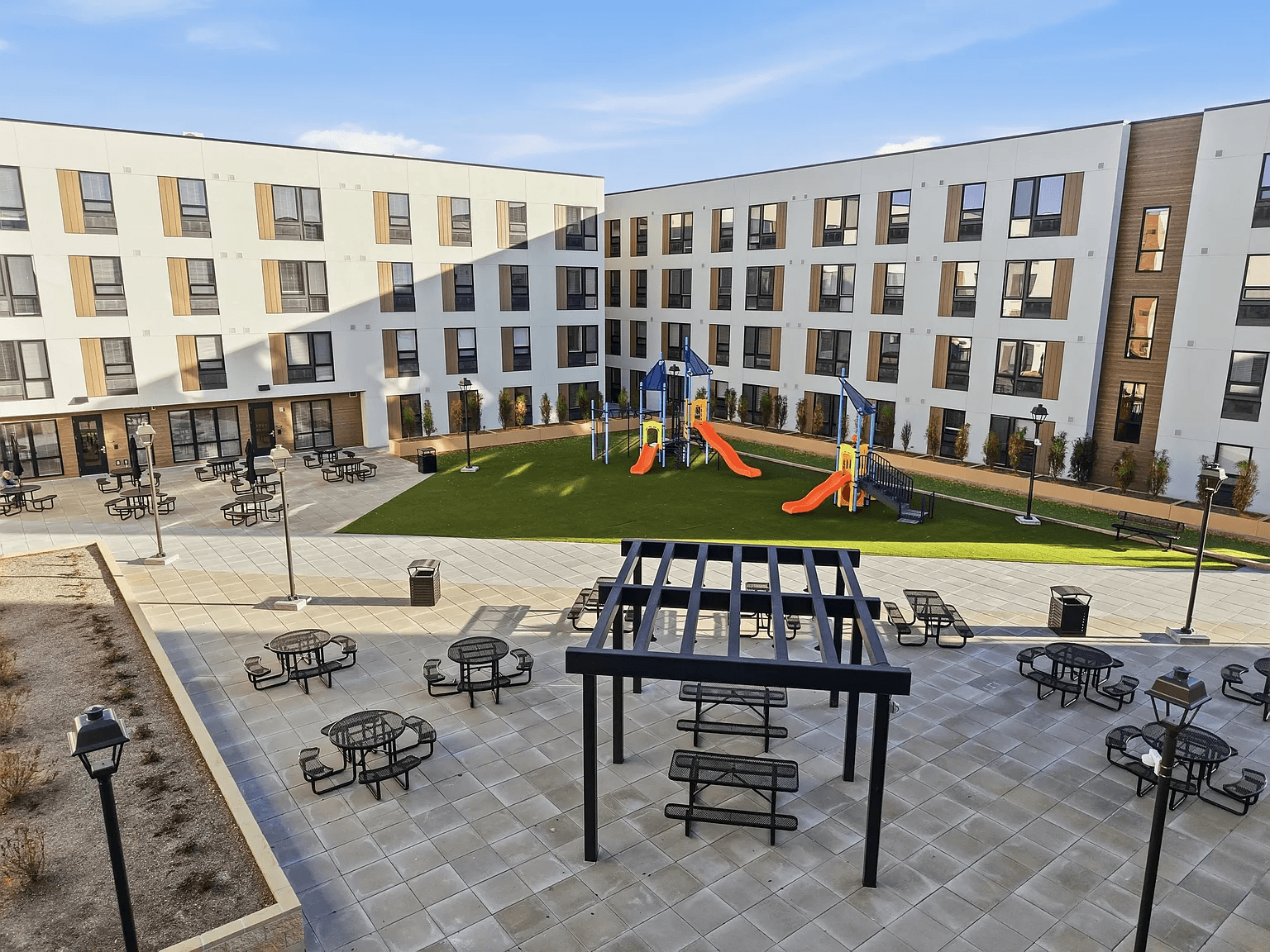 A playground area with a slide and picnic tables is surrounded by apartment buildings.